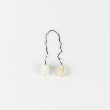 Das Bild zeigt zwei kleine, zylindrische Objekte, die durch einen Draht miteinander verbunden sind. Sie scheinen aus unterschiedlichen Materialien gefertigt zu sein und könnten für experimentelle Zwecke im Bildungsbereich verwendet werden.