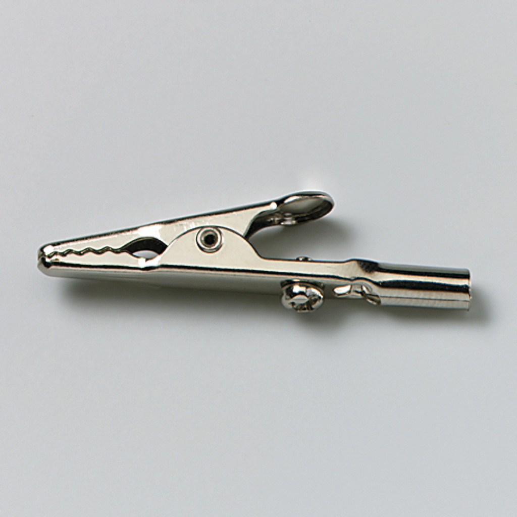 Das Bild zeigt eine metallische Krokodilklemme, die typischerweise in Experimenten verwendet wird. Sie dient zur elektrischen Verbindung von Bauteilen oder zur Befestigung von Drähten in der Wissenschaftsausbildung.