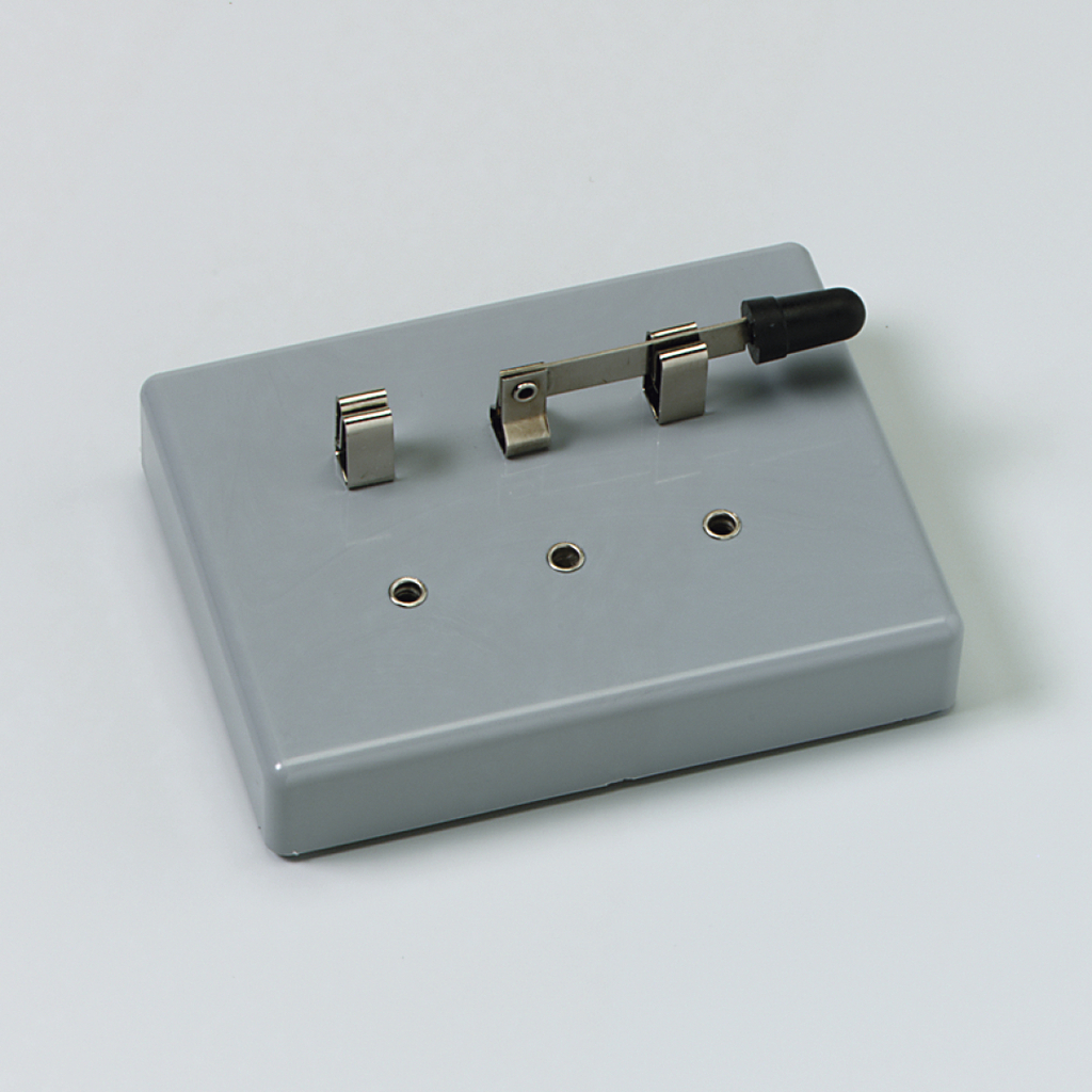 Das Bild zeigt ein graues Experimentiergerät mit zwei Metallkontakten und einem Schalter. Es dient wahrscheinlich zur Durchführung elektrischer Experimente im Bildungsbereich.