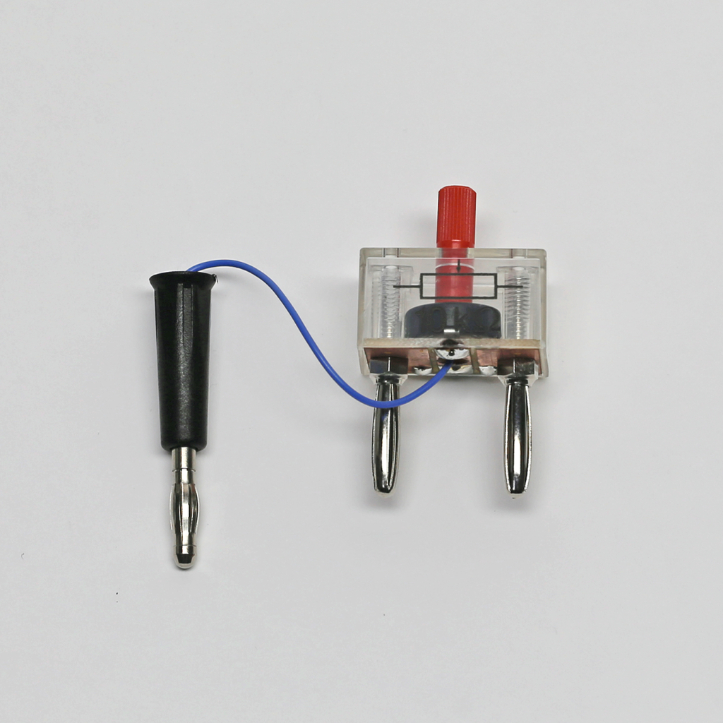 Das Bild zeigt ein elektrisches Experimentiergerät, das aus einem transparenten Gehäuse mit einem roten Drehknopf und zwei metallischen Kontaktpunkten besteht. Ein schwarzes Kabel mit einem steckbaren Anschluss ist an dem Gerät befestigt, was auf die Verwendung in wissenschaftlichen Experimenten hinweist.