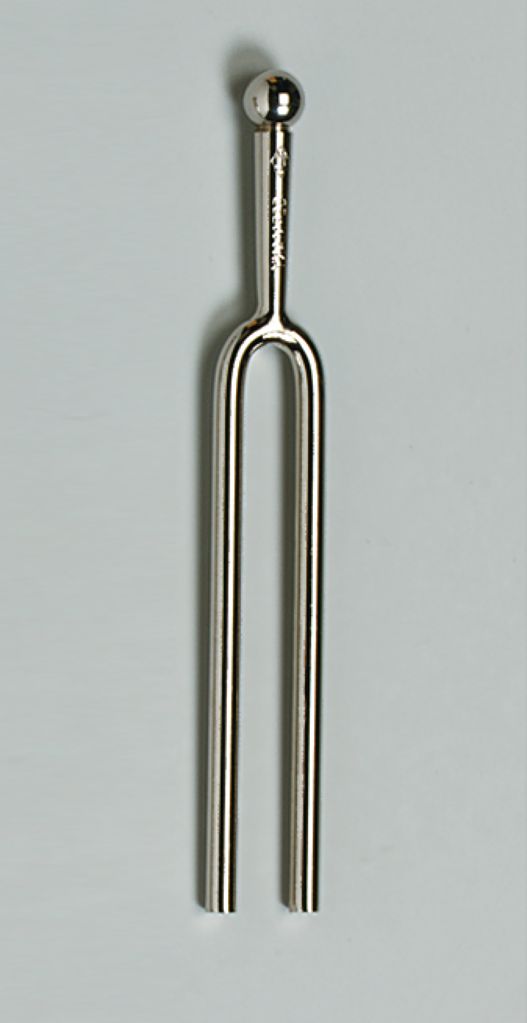 Das Bild zeigt ein Stahlgabel-Tonmittel, das aus einem langen, geschwungenen Metallrohr besteht, das oben mit einer kleinen Kugel endet. Es wird häufig in der Musikausbildung verwendet, um die Tonhöhe zu bestimmen und als Stimmgerät zu dienen.