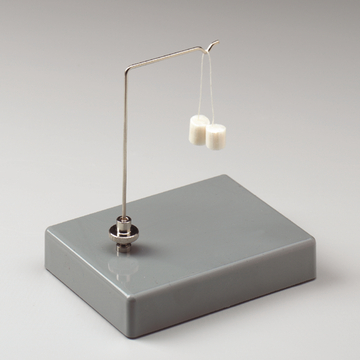 Das Bild zeigt eine einfache Hebelvorrichtung mit einem Metallbügel, der zwei kleine, weiße Gewichte trägt. Die Konstruktion steht auf einer grauen Basis und wird häufig für experimentspezifische Anwendungen im Bildungsbereich verwendet.