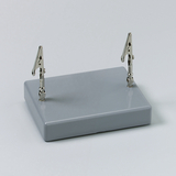 Das Bild zeigt eine graue Basisplatte mit zwei verstellbaren Klemmen, die aufrecht angebracht sind. Dieses Gerät wird häufig in Experimenten zur Befestigung von Materialien verwendet.