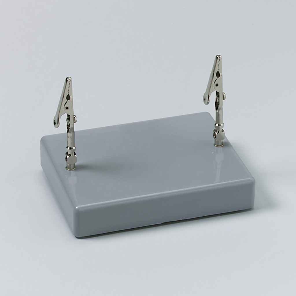 Das Bild zeigt eine graue Basisplatte mit zwei verstellbaren Klemmen, die aufrecht angebracht sind. Dieses Gerät wird häufig in Experimenten zur Befestigung von Materialien verwendet.