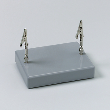 Das Bild zeigt eine graue Basisplatte mit zwei verstellbaren Klemmen, die aufrecht angebracht sind. Dieses Gerät wird häufig in Experimenten zur Befestigung von Materialien verwendet.