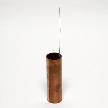 Das Bild zeigt einen zylindrischen Kupferbehälter mit einem dünnen Draht und einem kleinen schwarzen Objekt, das in der Öffnung hängt. Dieser Artikel könnte für Experimente in der Physik oder Chemie genutzt werden.
