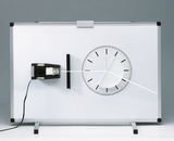 Das Bild zeigt ein Experimentiergerät, das zur Veranschaulichung von physikalischen Prinzipien eingesetzt wird. Es besteht aus einer weißen Tafel mit einer Skala und einer beweglichen Linie, die wahrscheinlich zur Messung von Winkeln oder Bewegungen dient.