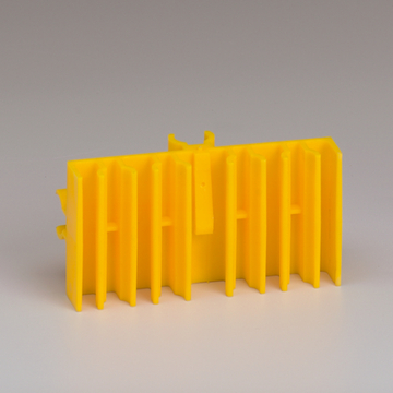 Das Bild zeigt ein leuchtend gelbes Experimentiergerät, das mehrere vertikale Rillen aufweist. Es scheint für Bildungszwecke im naturwissenschaftlichen Unterricht konzipiert zu sein.