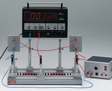 Das Bild zeigt ein digitales Multimeter, das mit elektrischen Komponenten verbunden ist, um verschiedene Messungen wie Stromstärke und Spannung durchzuführen. Neben dem Multimeter befindet sich ein Netzgerät zur Stromversorgung der Schaltung.