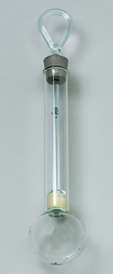 Das Bild zeigt einen Experimentierglasartikel, der aus einem langgestreckten Glasrohr mit einer halbkugelförmigen Basis besteht. Oben hat es einen geschlossenen Hals, der eine Aufhängemöglichkeit bietet, und im Inneren sind Materialien sichtbar, die für chemische Experimente genutzt werden können.