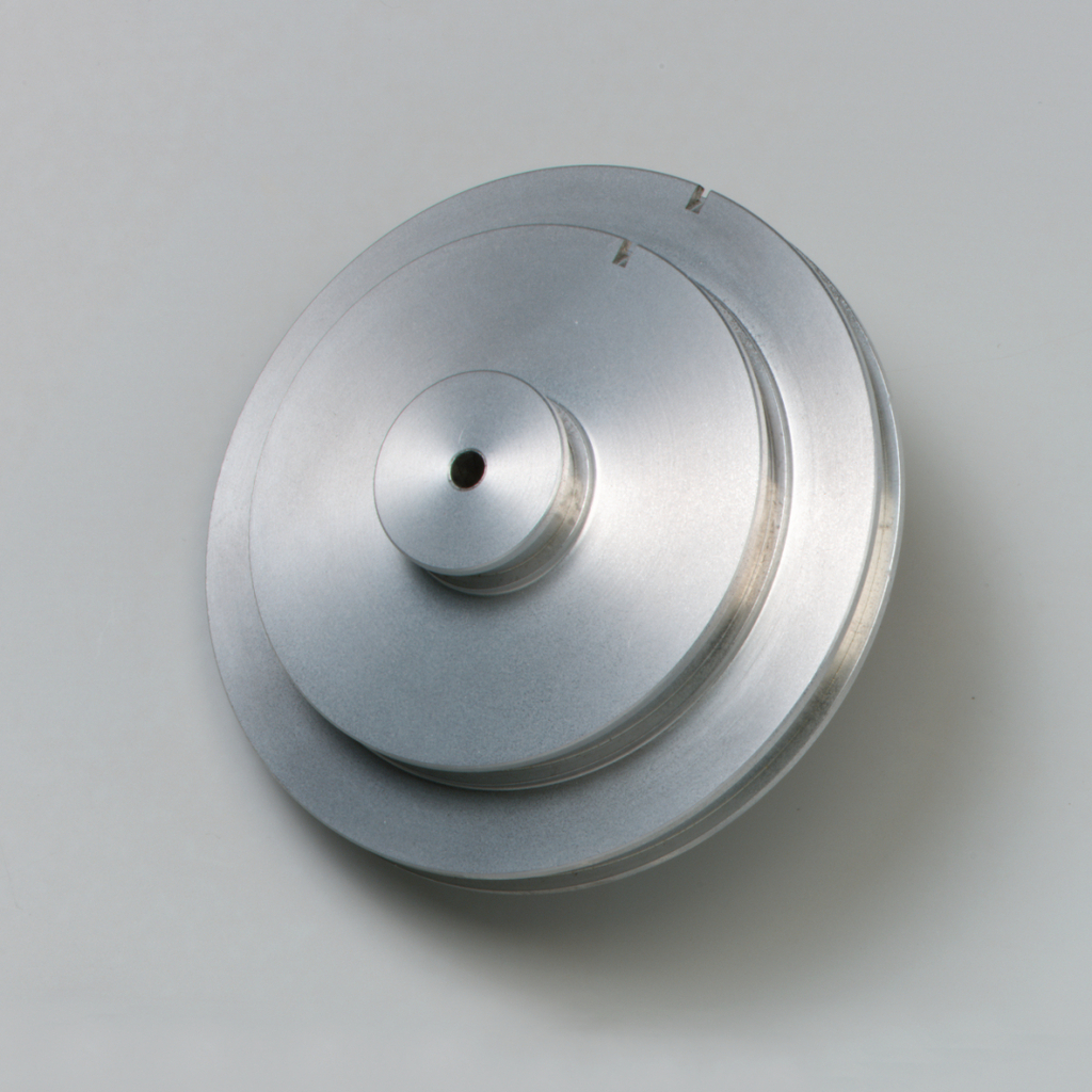 Das Bild zeigt ein silbernes, mehrlagiges Metallobjekt mit einer zentralen Bohrung, das wahrscheinlich für experimentelle Zwecke im Bildungswesen verwendet wird. Es hat eine glatte Oberfläche und eine präzise, runde Form, die auf eine technische Funktion hinweist.