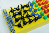 Das Bild zeigt ein Modell zur Darstellung von Molekülen, das aus verschiedenen bunten Kunststoffkugeln und Verbindungsstäben besteht. Die Elemente sind auf einer gelben Basis angeordnet, um chemische Strukturen anschaulich darzustellen.