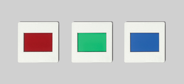 Das Bild zeigt drei rechteckige Farbscheiben, die in weißen Rahmen eingefasst sind. Die Farben sind von links nach rechts Rot, Grün und Blau, und sie könnten für Experimente in der Schule oder im Bildungsbereich verwendet werden.