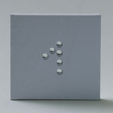 Das Bild zeigt eine graue Fläche mit mehreren kleinen, runden Objekten, die in einer bestimmten Anordnung platziert sind. Diese Objekte könnten Bestandteil eines Experimentierkits für den Bildungsbereich sein, möglicherweise zur Untersuchung physikalischer Phänomene.