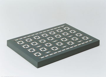 Das Bild zeigt eine graue Plattform mit einer Anordnung von metallenen Kontakten in rechteckiger Form. Diese Struktur könnte für Experimente im Bereich Elektronik oder Physik verwendet werden, um Stromkreise zu erstellen oder zu untersuchen.