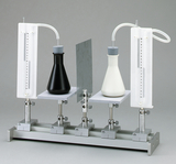 Das Bild zeigt eine Apparatur mit zwei Erlenmeyerkolben, einem schwarzen und einem weißen, die an einem stabilen Stand befestigt sind. An jedem Kolben sind Messröhren angeschlossen, die zur Durchführung von Experimenten im Bildungsbereich geeignet sind.