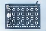 Das Bild zeigt eine experimentelle Plattform mit einer Vielzahl von runden Löchern in einem Gittermuster, die zur Verdrahtung genutzt werden können. An der Oberseite sind Anschlüsse für Plus- und Minus-Polaritäten zu sehen, um Schaltungen zu erstellen.