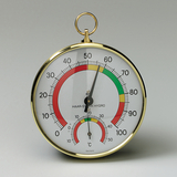 Das Bild zeigt ein analoges Thermo-Hygrometer mit einer goldenen Rahmenkonstruktion. Es misst die Temperatur in Grad Celsius und die Luftfeuchtigkeit, dargestellt durch eine farbige Skala in Grün, Gelb und Rot.