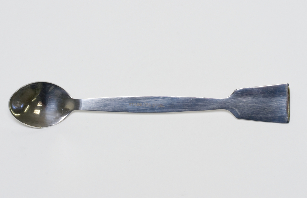 Das Bild zeigt einen Edelstahl-Löffel mit einer flachen, breiten Seite und einer ovalen Löffelform. Dieser Löffel könnte für Experimente in der Schule oder im Labor eingesetzt werden, um verschiedene Substanzen zu mischen oder zu bewegen.