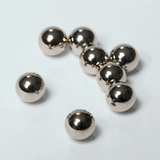 Das Bild zeigt mehrere glänzende Metallkugeln, die auf einer hellen Oberfläche verstreut sind. Diese Kugeln könnten für chemische Experimente oder physikalische Aufgaben im Bildungswesen verwendet werden.