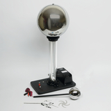 Das Bild zeigt ein elektrostatisches Gerät, wie eine Van-de-Graaff-Generatoranlage, mit einer großen Metallkugel auf einem stabilen Unterbau. Neben dem Gerät befinden sich verschiedene Zubehörteile, die für Experimente im Bildungsbereich verwendet werden können.