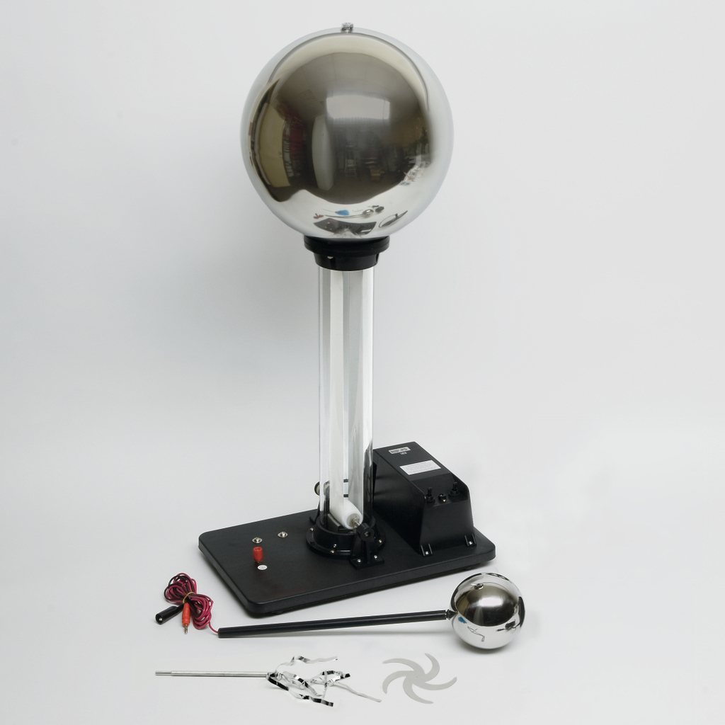 Das Bild zeigt ein elektrostatisches Gerät, wie eine Van-de-Graaff-Generatoranlage, mit einer großen Metallkugel auf einem stabilen Unterbau. Neben dem Gerät befinden sich verschiedene Zubehörteile, die für Experimente im Bildungsbereich verwendet werden können.