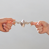 Das Bild zeigt zwei Hände, die jeweils einen Klemmenhalter mit einer transparenten Linse halten. Die Halter sind an beiden Enden verbunden und scheinen ein Experiment oder eine Demonstration zu unterstützen.