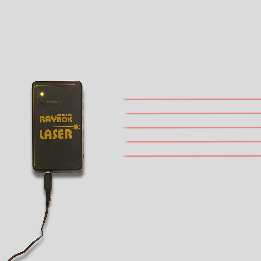 Das Bild zeigt ein kompaktes Gerät mit der Bezeichnung "electronic RAYBOX LASER", das einen Laserstrahl erzeugt. Der Strahl wird in mehreren roten Linien dargestellt, die sich vom Gerät nach rechts erstrecken.