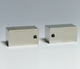 Das Bild zeigt zwei rechteckige Metallblöcke, die eine polierte Oberfläche haben und jeweils ein Loch auf einer der Seiten aufweisen. Diese Blöcke könnten für physikalische Experimente oder für den Einsatz in der Bildungsforschung verwendet werden.
