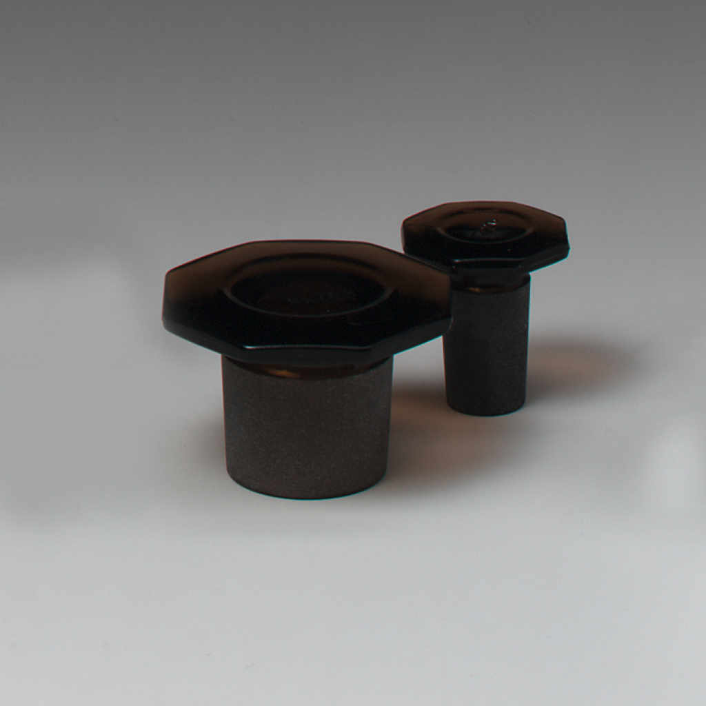 Auf dem Bild sind zwei experimentelle Ausstattungen zu sehen, die aus einem schwarzen Material gefertigt sind. Die Objekte haben eine zylindrische Form mit einer breiten, hexagonalen Oberseite und variieren in der Höhe.