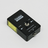 Das Bild zeigt ein schwarzes Gerät mit der Aufschrift "Cornelsen Experimenta", das als Schaltgerät fungiert. Es verfügt über einen Schalter für einen Laser und eine LED-Anzeige, mit einem Anschluss für eine maximal 3V Stromversorgung.