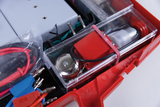 Das Bild zeigt eine praktische Kiste, die mit verschiedenen Experimentiermaterialien ausgestattet ist, darunter Kabel, Kontakte und ein Mechanismus. Diese Materialien sind für den Einsatz im Bildungsbereich konzipiert, um Schülern experimentelles Lernen zu ermöglichen.