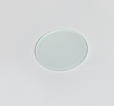 Das Bild zeigt eine durchsichtige, runde Objektträgerplatte aus Glas, die auf einem weißen Untergrund liegt. Diese Platte wird häufig in wissenschaftlichen Experimenten und bei mikroskopischen Untersuchungen verwendet.