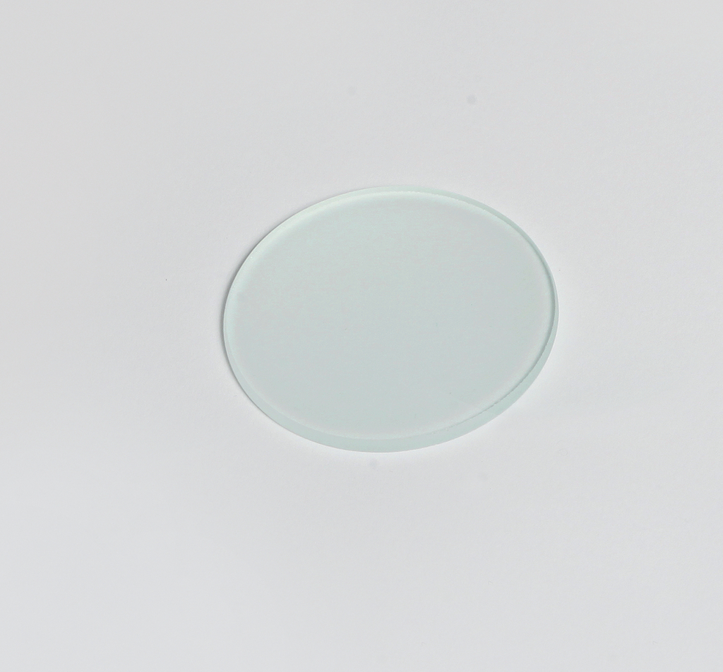 Das Bild zeigt eine durchsichtige, runde Objektträgerplatte aus Glas, die auf einem weißen Untergrund liegt. Diese Platte wird häufig in wissenschaftlichen Experimenten und bei mikroskopischen Untersuchungen verwendet.