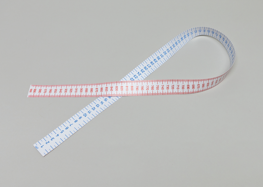 Das Bild zeigt ein flexibles Maßband, das auf einer neutralen Oberfläche liegt. Es ist auf der einen Seite blau und auf der anderen Seite rot, mit klaren numerischen Markierungen für präzise Messungen.