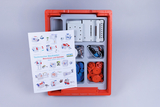Das Bild zeigt einen technischen Baukasten mit verschiedenen Bauteilen wie Zahnrädern, Motoren und Montageteilen, die in einer roten Box organisiert sind. Außerdem liegt eine Anleitung bei, die mehrere Modelle und deren Anwendung beschreibt.