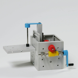 Das Bild zeigt ein mechanisches Modell mit Zahnrädern und einer Hebelmechanik, das für experimentelle Zwecke im Bildungsbereich entwickelt wurde. Es besteht aus grauem Material mit farbigen Zahnrädern in Rot und Gelb sowie einem blauen Hebel.