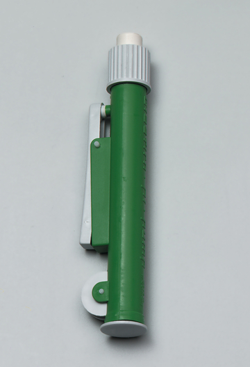 Das Bild zeigt ein grünes Experimentiergerät, das eine zylindrische Form mit einem weißen oberen Ende hat. An der Seite befindet sich eine silberne Klammer, die für die Befestigung an einem Objekt verwendet werden kann.