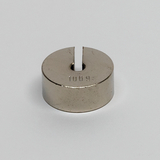 Das Bild zeigt einen runden, metallischen Block mit einer Vertiefung und einer Spalte in der Mitte, auf dem die Zahl "100 g" eingraviert ist. Dieses Objekt dient vermutlich als Gewicht für Experimente im Bildungswesen.