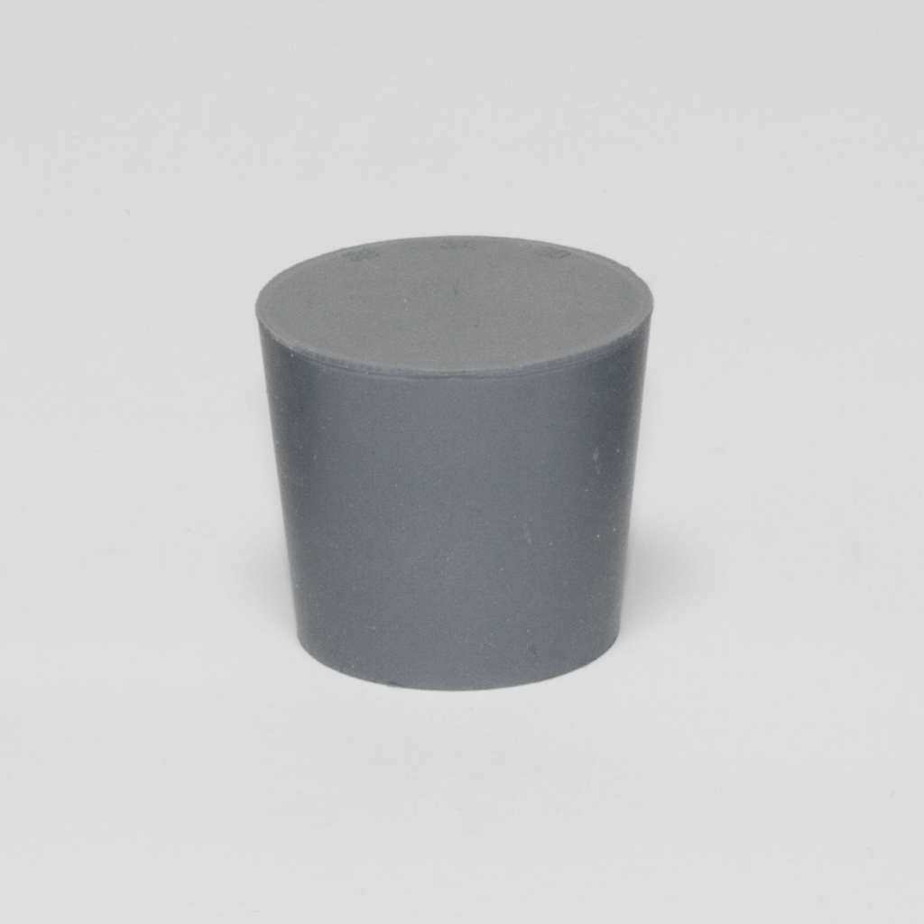 Das Bild zeigt einen grauen, zylindrischen Block aus Kunststoff mit einer flachen Oberseite. Dieses Experimentiermaterial könnte in verschiedenen wissenschaftlichen Anwendungen im Bildungsbereich verwendet werden.