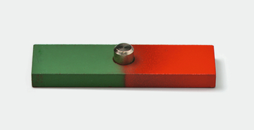 Das Bild zeigt ein rechteckiges Experimentierobjekt, das zur Veranschaulichung von Magnetfeldern verwendet wird. Es hat eine grüne und eine rote Seite sowie einen Metallzylinder in der Mitte.