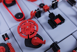 Das Bild zeigt eine Anordnung von Experimentierbausteinen in Rot und Schwarz, die für technische oder physikalische Experimente verwendet werden können. Die Komponenten scheinen Teile eines modularen Systems zu sein, das verschiedene Mechanismen oder Maschinen simuliert.