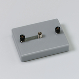 Das Bild zeigt ein graues Experimentiergerät mit zwei Anschlüssen, einem schwarzen und einem silbernen, verbunden durch eine Metallstrebe. Es ist vermutlich für den Einsatz im Bildungsbereich zur Durchführung von physikalischen Experimenten gedacht.