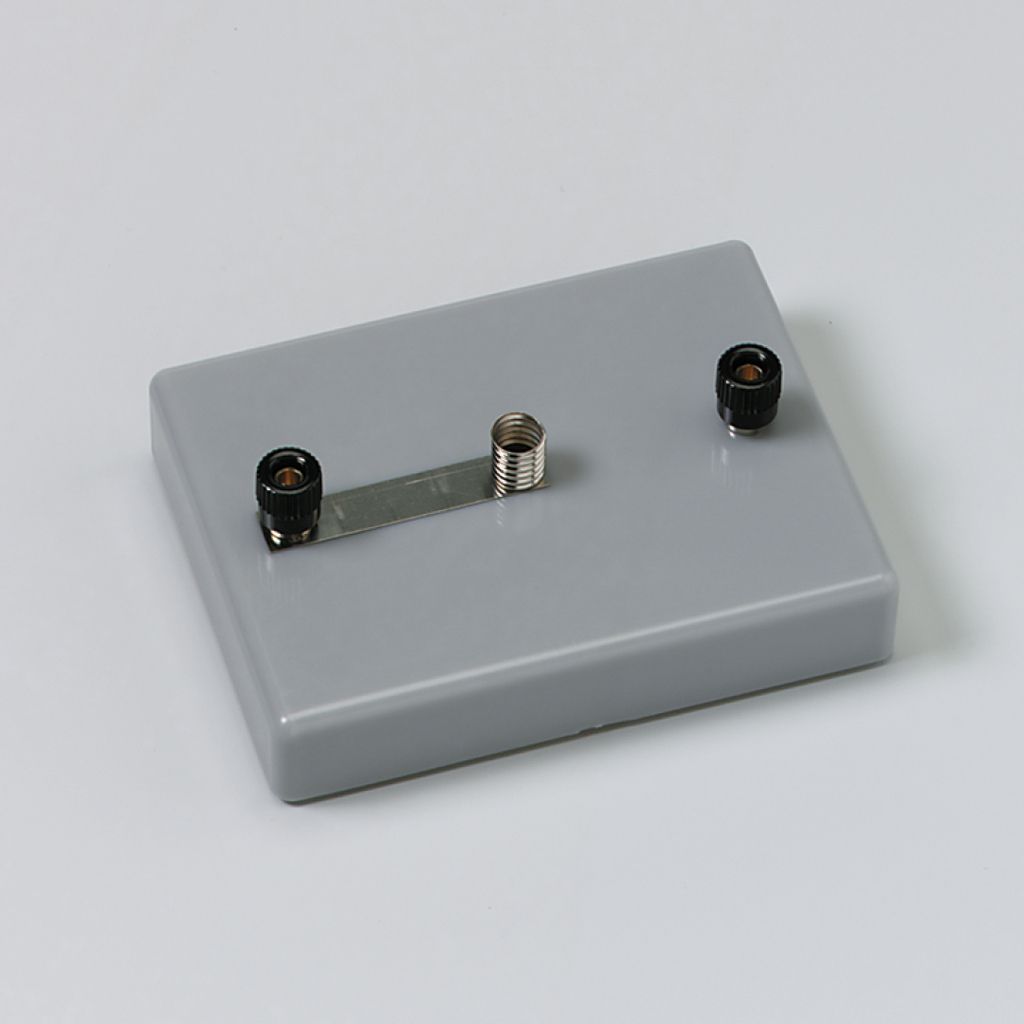 Das Bild zeigt ein graues Experimentiergerät mit zwei Anschlüssen, einem schwarzen und einem silbernen, verbunden durch eine Metallstrebe. Es ist vermutlich für den Einsatz im Bildungsbereich zur Durchführung von physikalischen Experimenten gedacht.