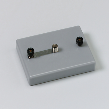 Das Bild zeigt ein graues Experimentiergerät mit zwei Anschlüssen, einem schwarzen und einem silbernen, verbunden durch eine Metallstrebe. Es ist vermutlich für den Einsatz im Bildungsbereich zur Durchführung von physikalischen Experimenten gedacht.