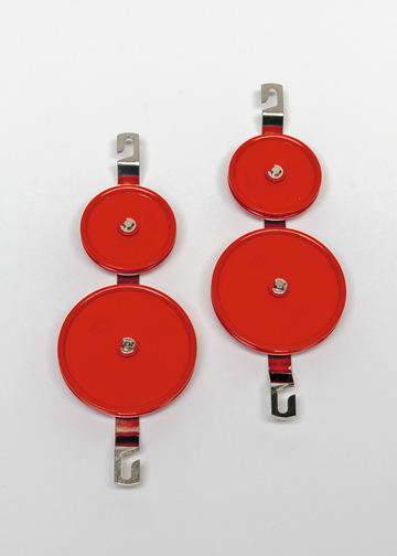 Das Bild zeigt zwei rot lackierte Scheiben mit Halterungen, die vermutlich für experimentelle Zwecke im Bildungswesen gedacht sind. Jede Scheibe hat eine zentrale Schraube und eine Metallbefestigung, die eine einfache Handhabung ermöglicht.