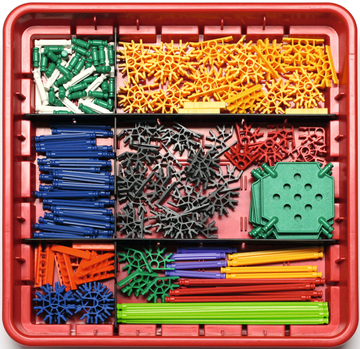 Das Bild zeigt eine Vielzahl von farbigen Experimentierbausteinen, die in einem roten Behälter organisiert sind. Die Bauteile bestehen aus unterschiedlichen Formen und Farben, die für Bildungszwecke und Experimentieren verwendet werden können.