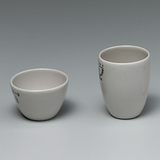 Das Bild zeigt zwei weiße Keramiktöpfe, einen kleineren, runden Behälter und einen höheren, schmaleren Becher. Beide Töpfe sind unbedruckt, mit klaren Kanten und in einem schlichten, funktionalen Design gehalten.