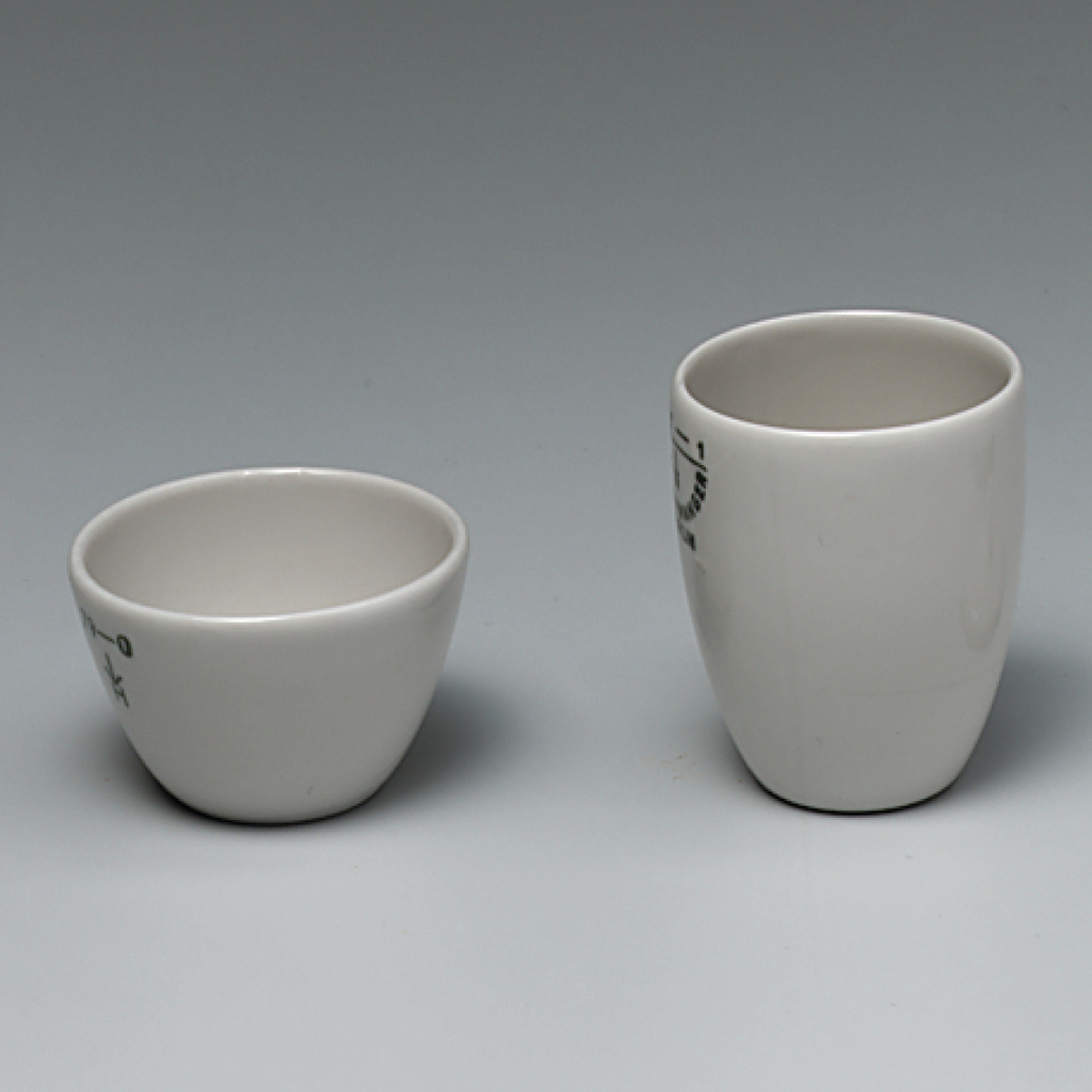 Das Bild zeigt zwei weiße Keramiktöpfe, einen kleineren, runden Behälter und einen höheren, schmaleren Becher. Beide Töpfe sind unbedruckt, mit klaren Kanten und in einem schlichten, funktionalen Design gehalten.