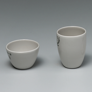 Das Bild zeigt zwei weiße Keramiktöpfe, einen kleineren, runden Behälter und einen höheren, schmaleren Becher. Beide Töpfe sind unbedruckt, mit klaren Kanten und in einem schlichten, funktionalen Design gehalten.